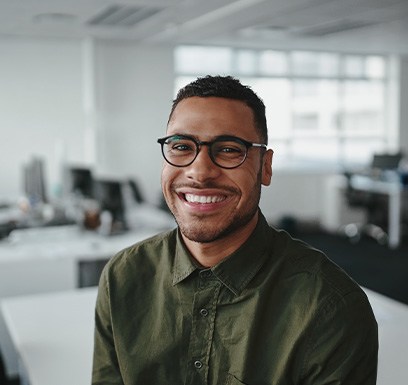 a smiling man sitting on a desk in an office