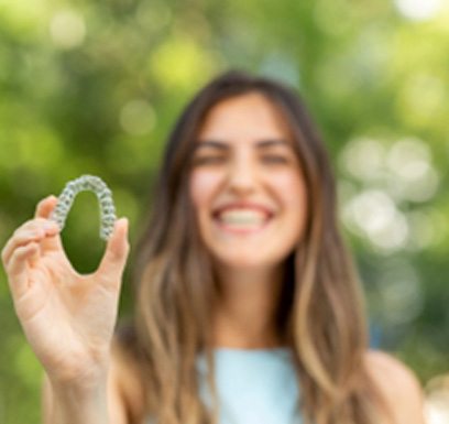 Smiling patient holding Invisalign clear aligner outside