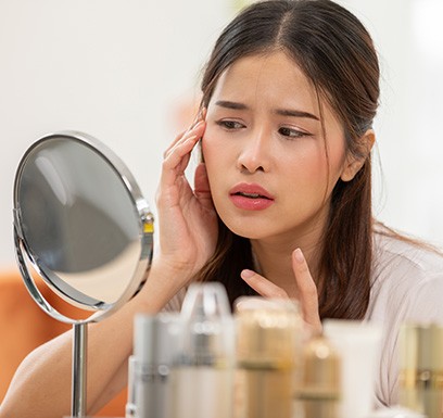 Woman looking at her face in mirror, concerned about wrinkles