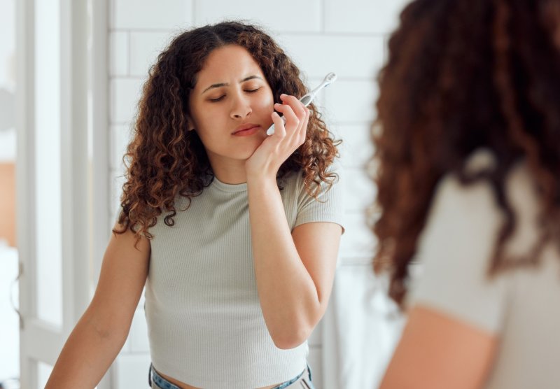 young woman with tooth pain while brushing teeth